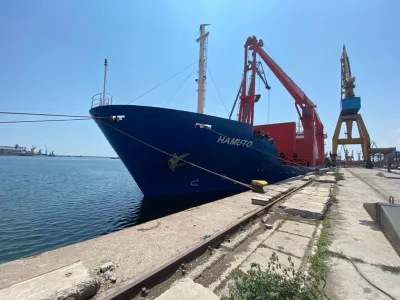 Geared general cargo vessel alongside the quay with her deck cranes raised